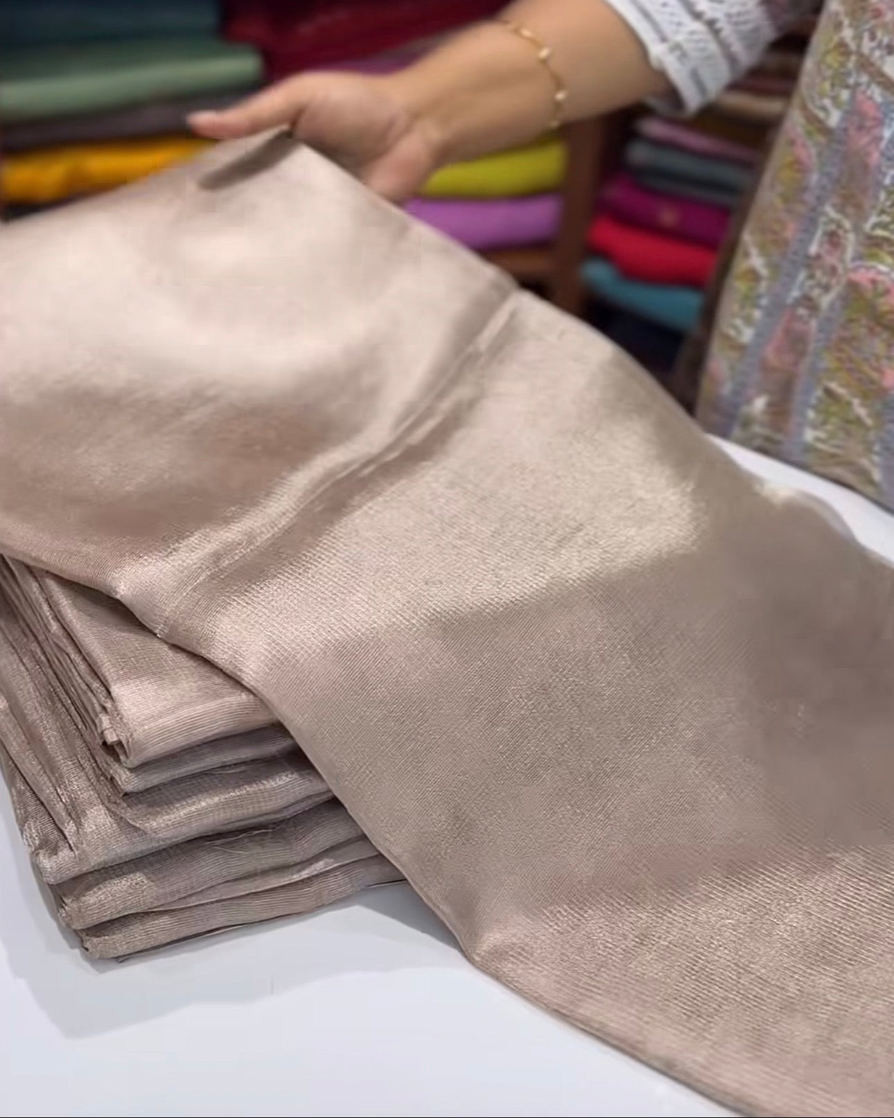 Beige fabric held by a person with colorful fabrics in the background