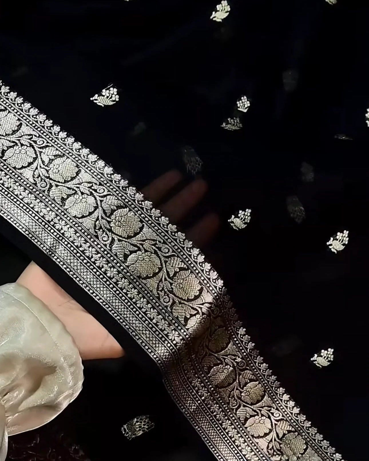 Close-up of a black fabric with silver embroidery and a white flower.