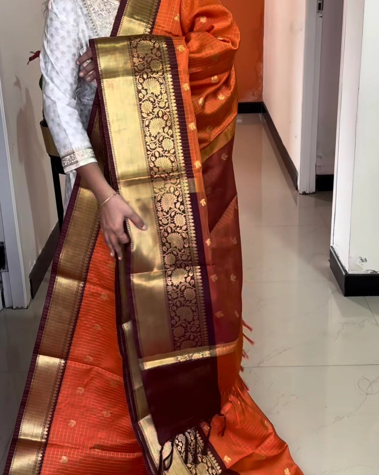 Person wearing an orange saree with gold border indoors.
