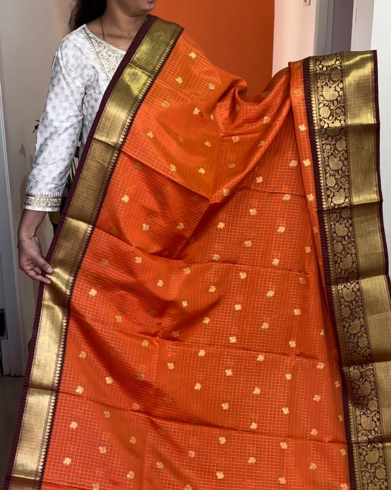 Orange saree with gold border draped over a person, against an orange wall.