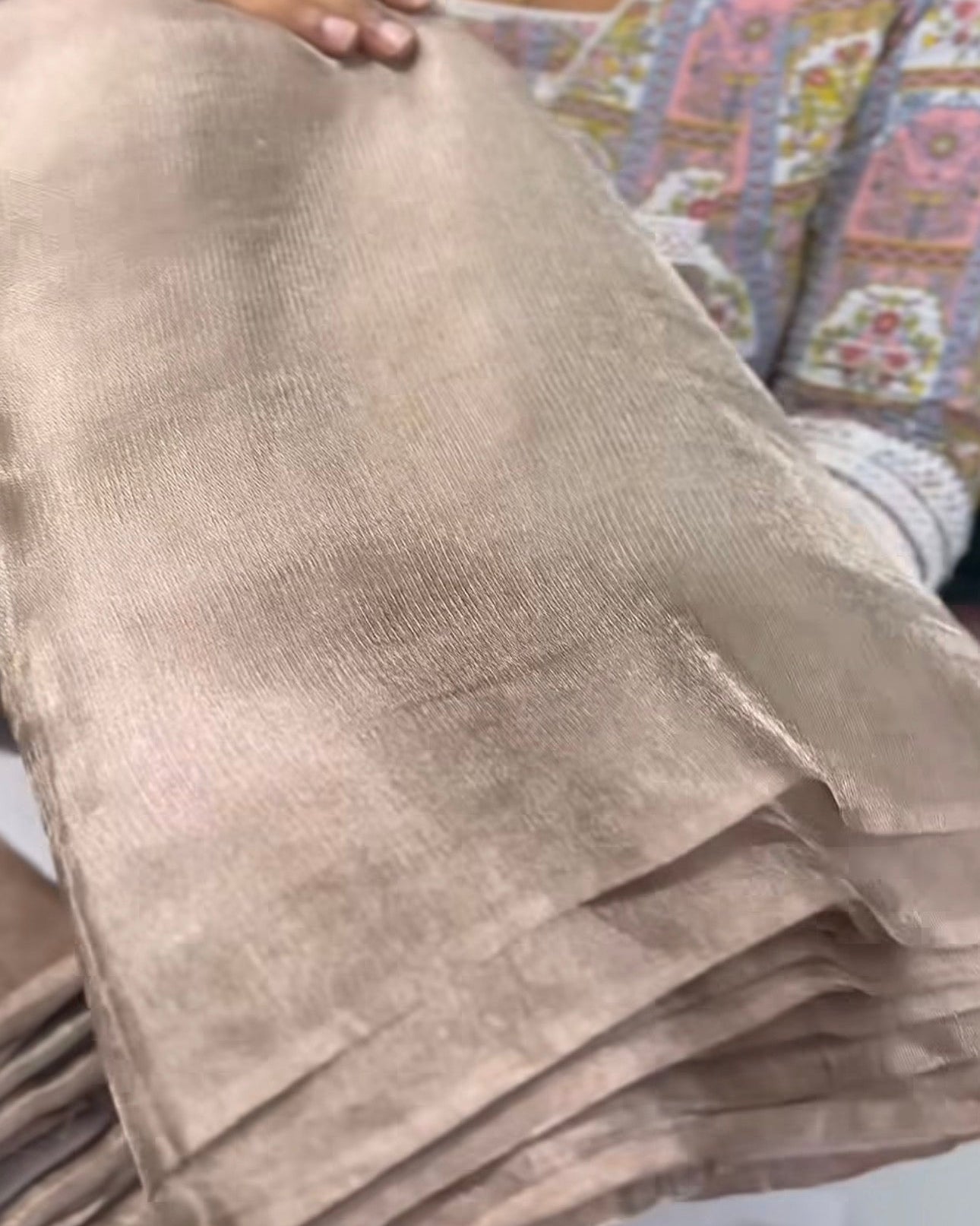 Beige fabric held by a person with a patterned background