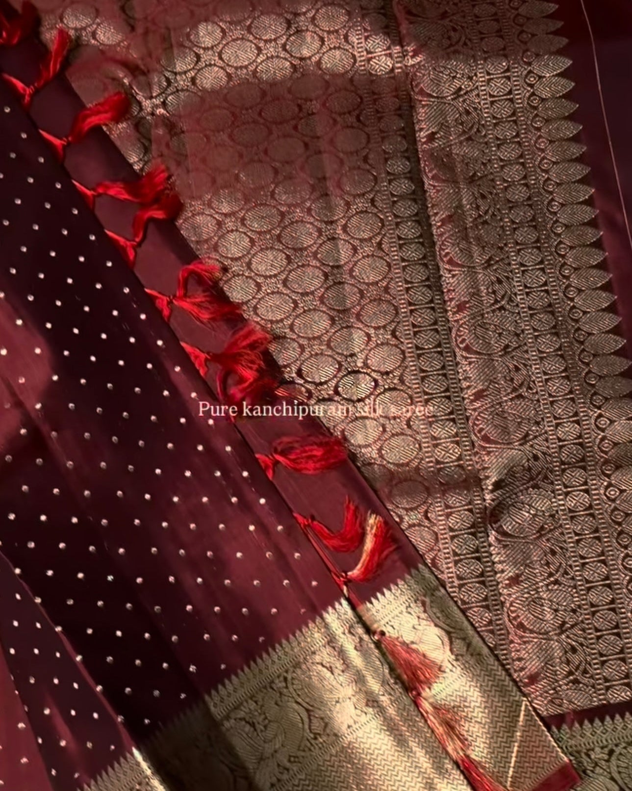 Close-up of a maroon saree with white polka dots and red border, featuring intricate patterns.