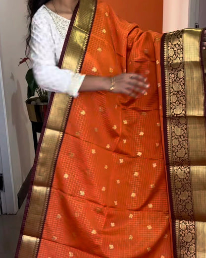 Person wearing an orange saree with a gold border indoors.
