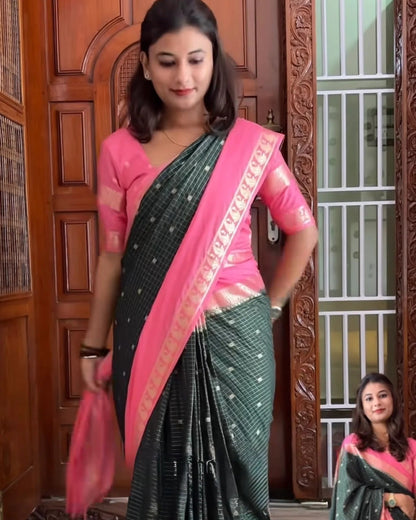 A woman modeling a Mysore crepe silk zip & go saree with a pink blouse, standing in front of a carved wooden door. The saree is dark green with a pink border and small white motifs.