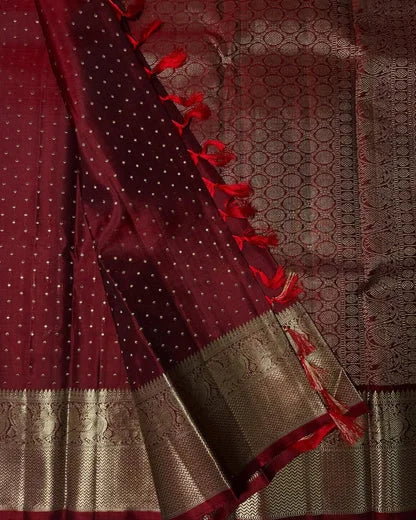 Maroon saree with gold border and red tassels on a textured fabric background