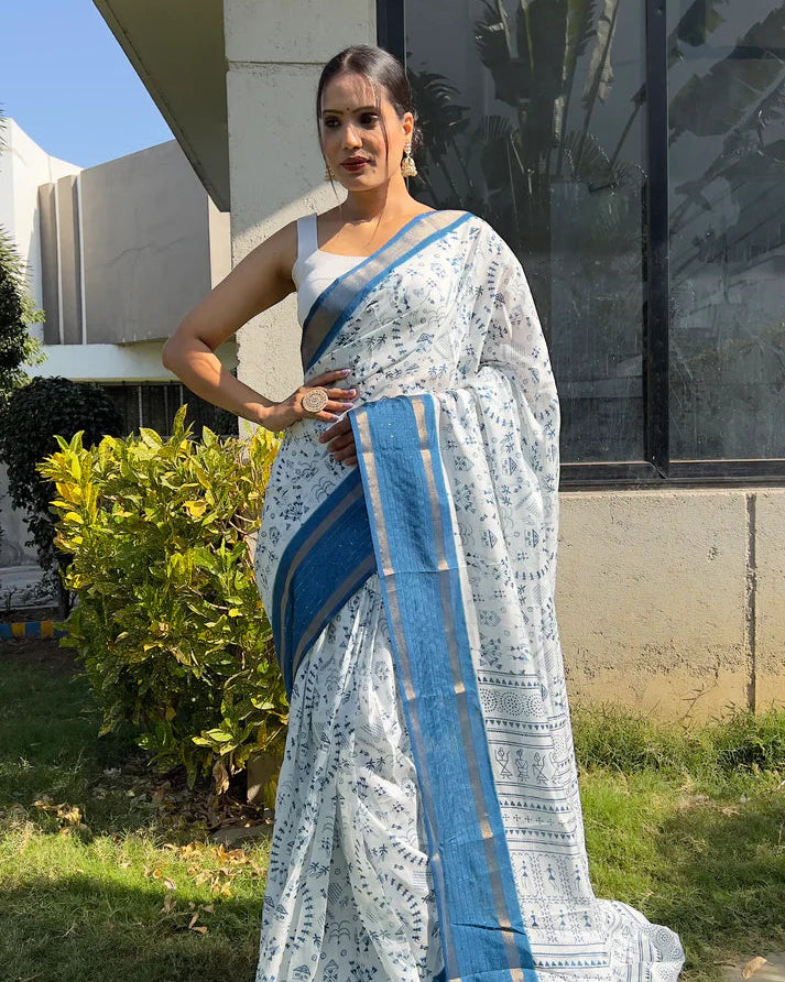 Woman in a white saree with blue stripes standing outdoors.