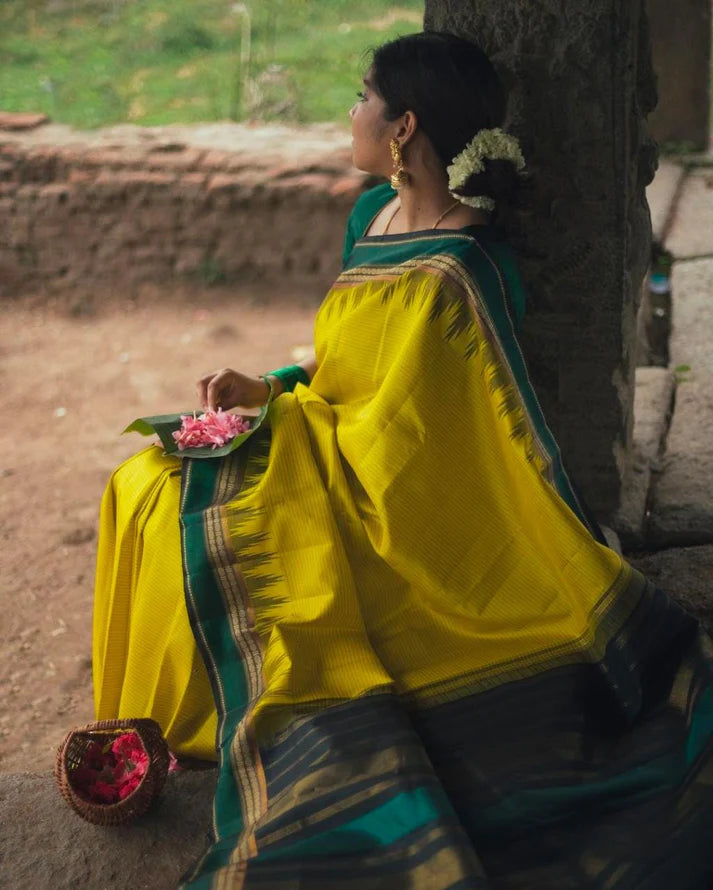 Woman in a yellow saree sitting against a stone wall with a natural background