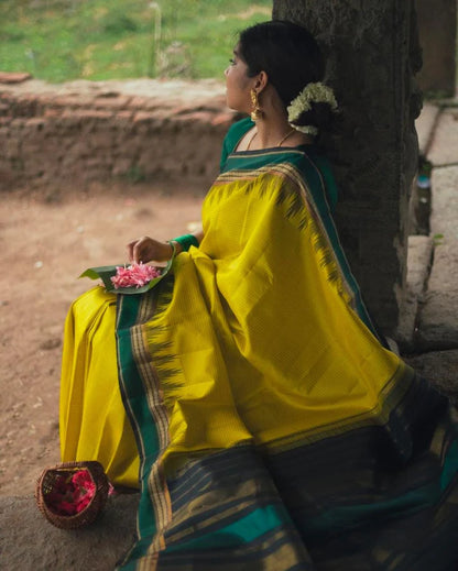 Woman in a yellow saree sitting against a stone wall with a natural background