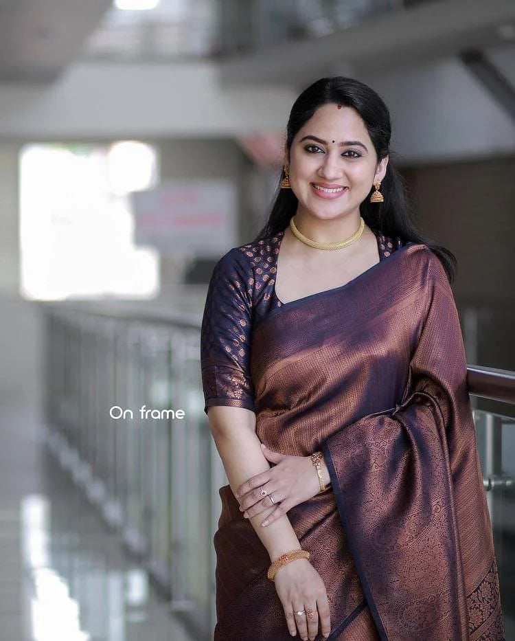 Woman in a brown saree standing indoors with a blurred background