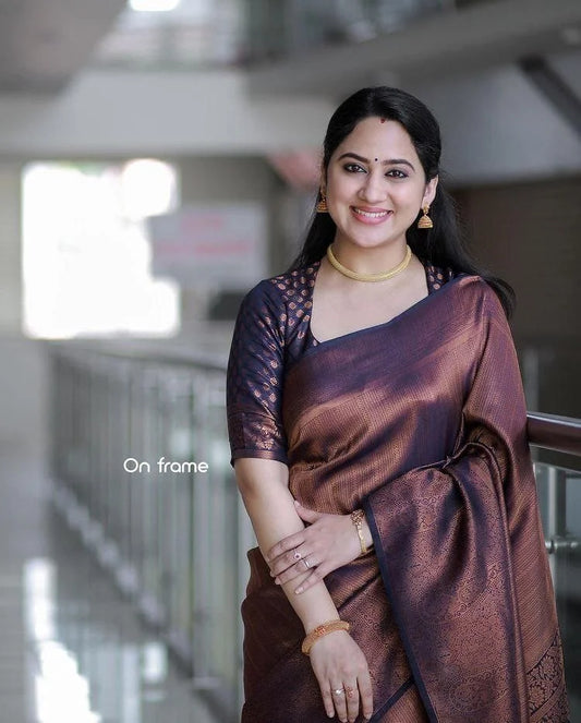 Woman in a brown saree standing indoors with a blurred background