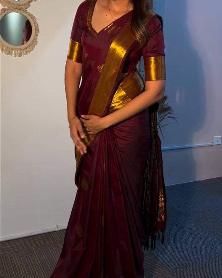 Woman in a maroon saree with gold border standing indoors.