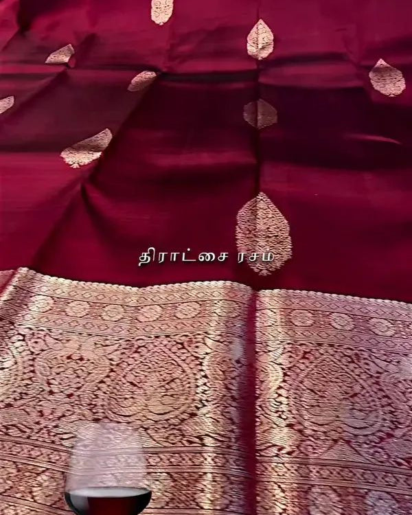Maroon fabric with gold patterns and a glass of red wine on a white surface