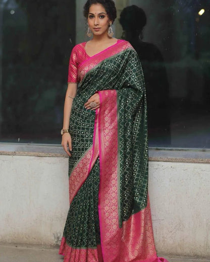 Woman wearing a green and pink saree against a reflective glass wall.
